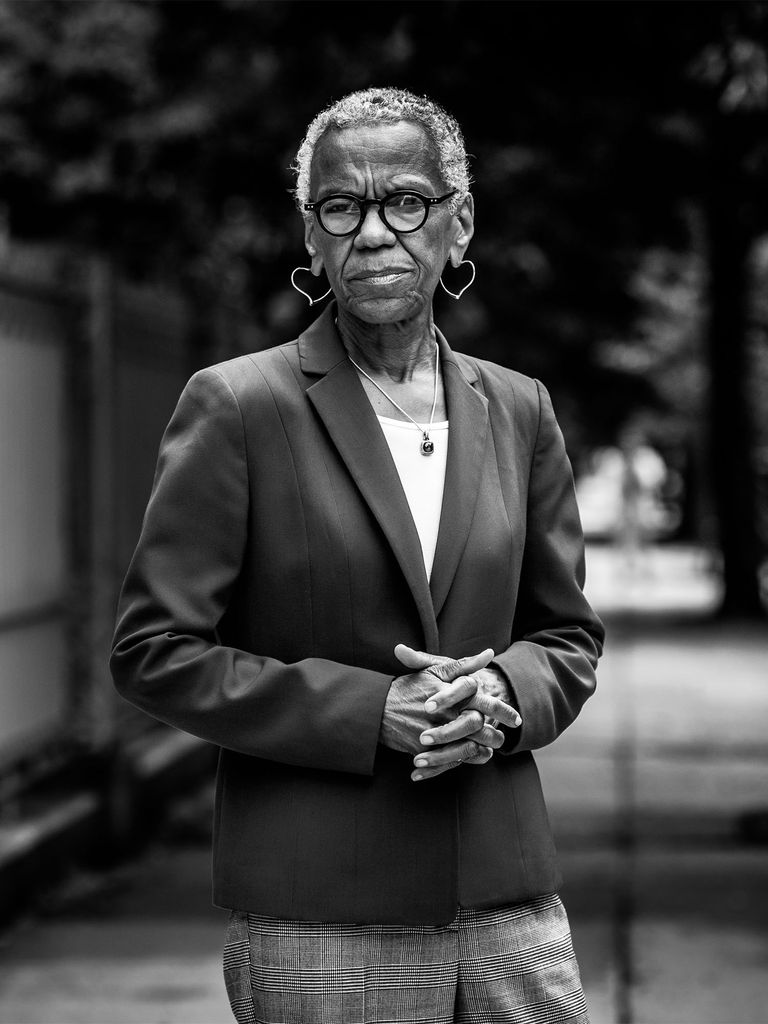 Andrea Taylor stands with hands clasped outdoors in a suit jacket in this black and white photo