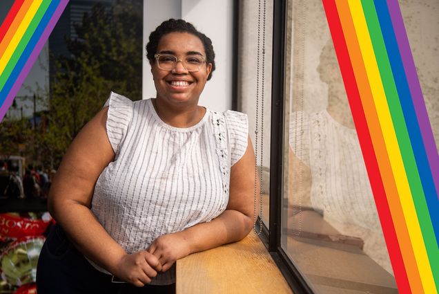 Photo of Chantel James, a young Black woman with clear glasses. She smiles, and wears a white blouse with tufted sleeves. She leans against a window in a room, presumably an office. Small pastel-colored rainbows are overlaid at left and right of the photo.