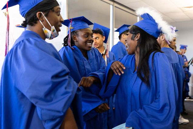 Photo of Charlestown High School senior Chakaiya Harrison (center), a Menino Scholar and Charlestown High School’s Class of 2022 school's salutatorian, doing quick dance with her friends, Kaemani Hammonds, left, and Marley Gustama on Wednesday, June 22, 2022 before or after the ceremony. The students pictured are all young people of color and they wear bright blue caps and gowns as they smile and laugh together.