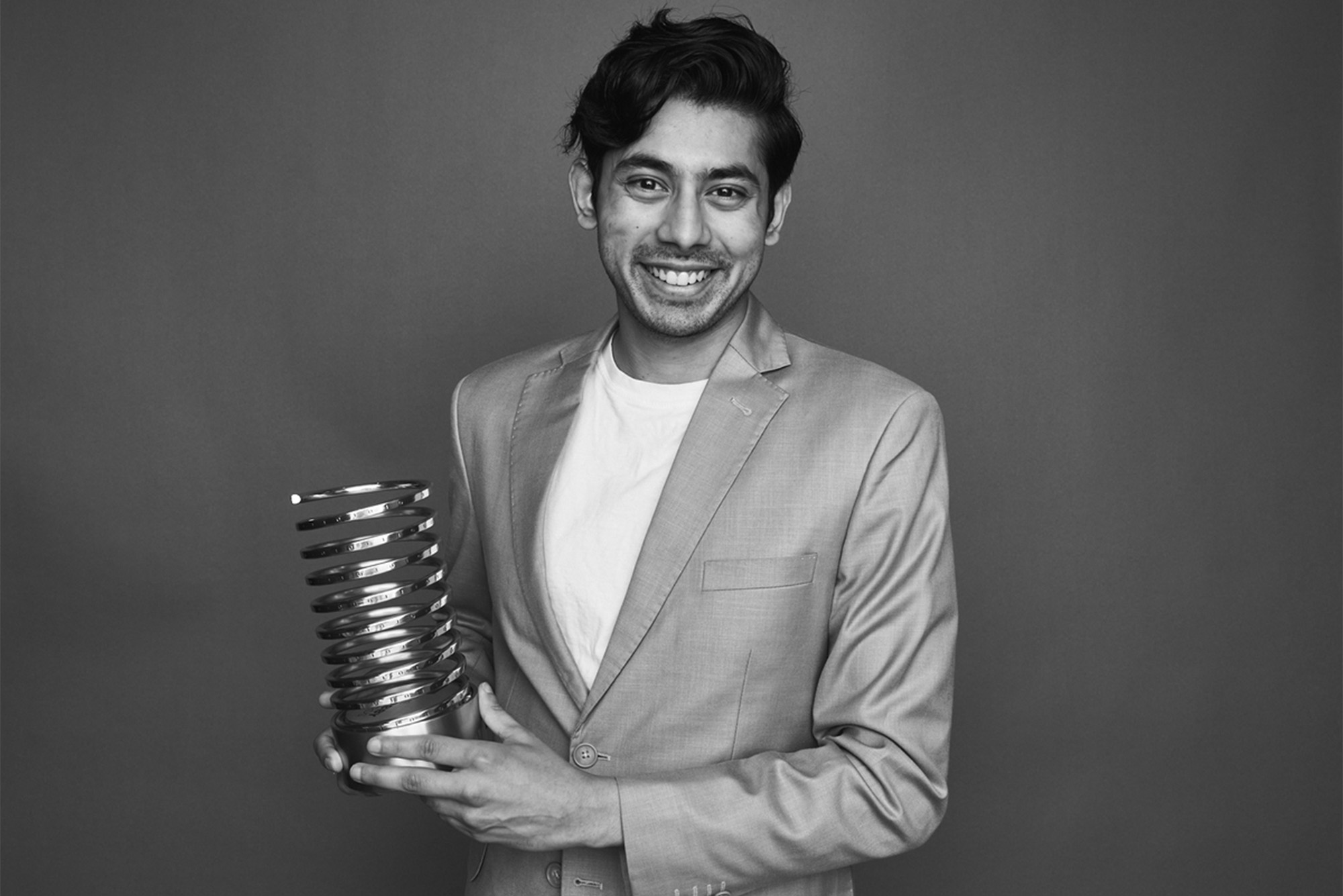 Rohan Gupta with his Webby Award in hand. He is wearing a grey suit and a white undershirt