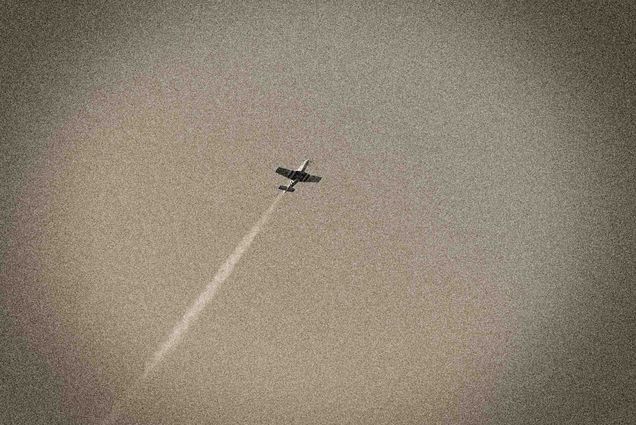 A WWII era plane flies through the sky with a vapor trail behind