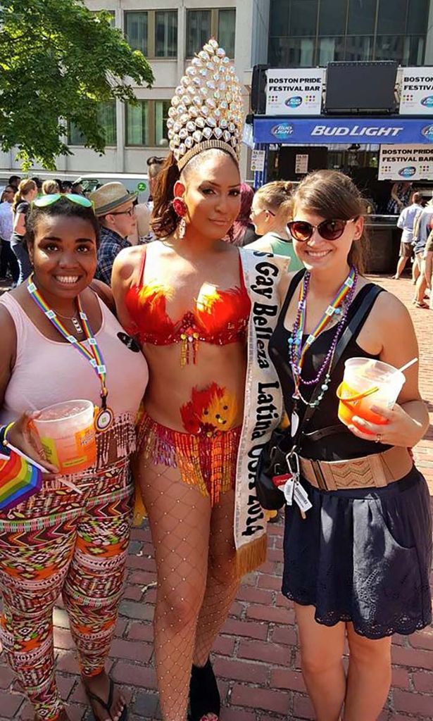 Photo of Chantel James, at left, at Boston Pride, a few years ago. James wears colorful patterned pants, a pink tank top and a rainbow necklace, and holds a large drink presumably. At center, is a person with a large tiara and outfit with red sequins and sparkling fishnets. They wear a sash that reads "Gay Belleza Latina". At right, a lighter skinned woman with sunglasses on smiles and wears a black dress. Other pride attendees are seen behind them.