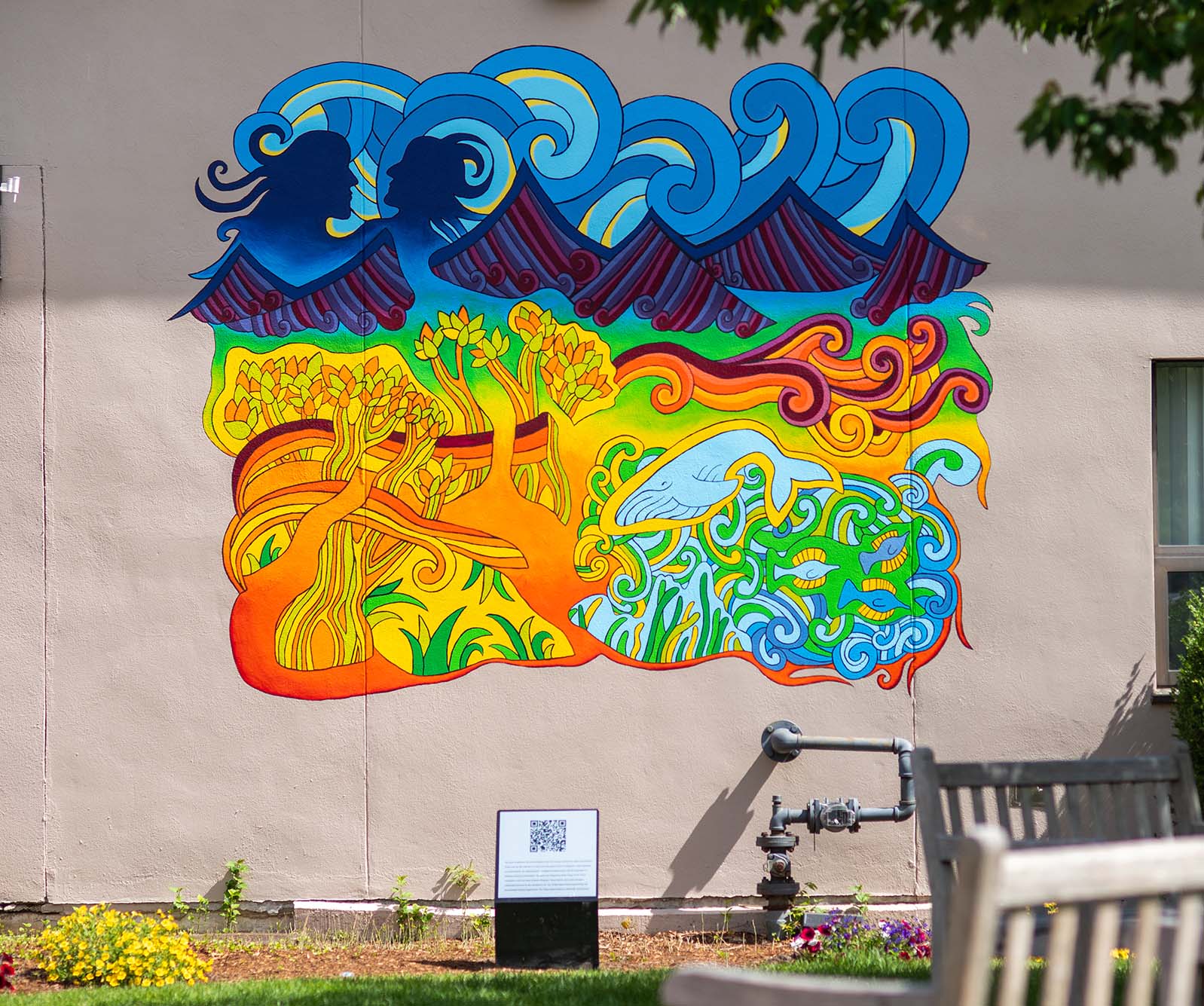 Photo of a completed mural on the Kenmore Building. Mural depicts a colorful, rainbow mishmash of nature - waves, a whale, mountains, fish, wind, and trees.