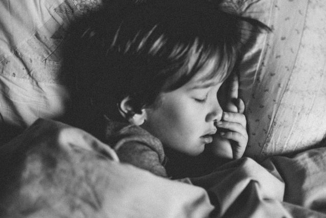 Black and white photo of a young child sleeping in a bed.