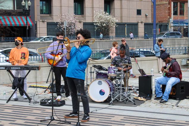 A band with drums, trombone, bass, and keys plays in Boston on an overcast day