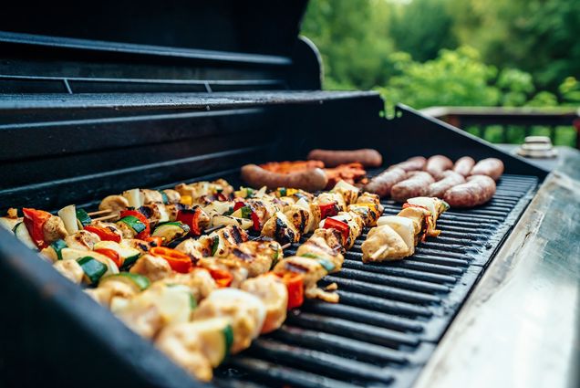 Photo of chicken kebabs and sausages on a propane grill.