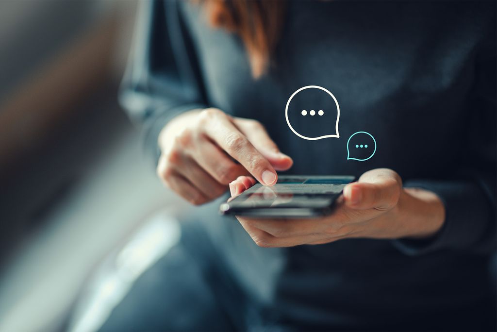 A person texts on a mobile phone, with floating message bubbles above the phone. Photo by iStock/oatawa