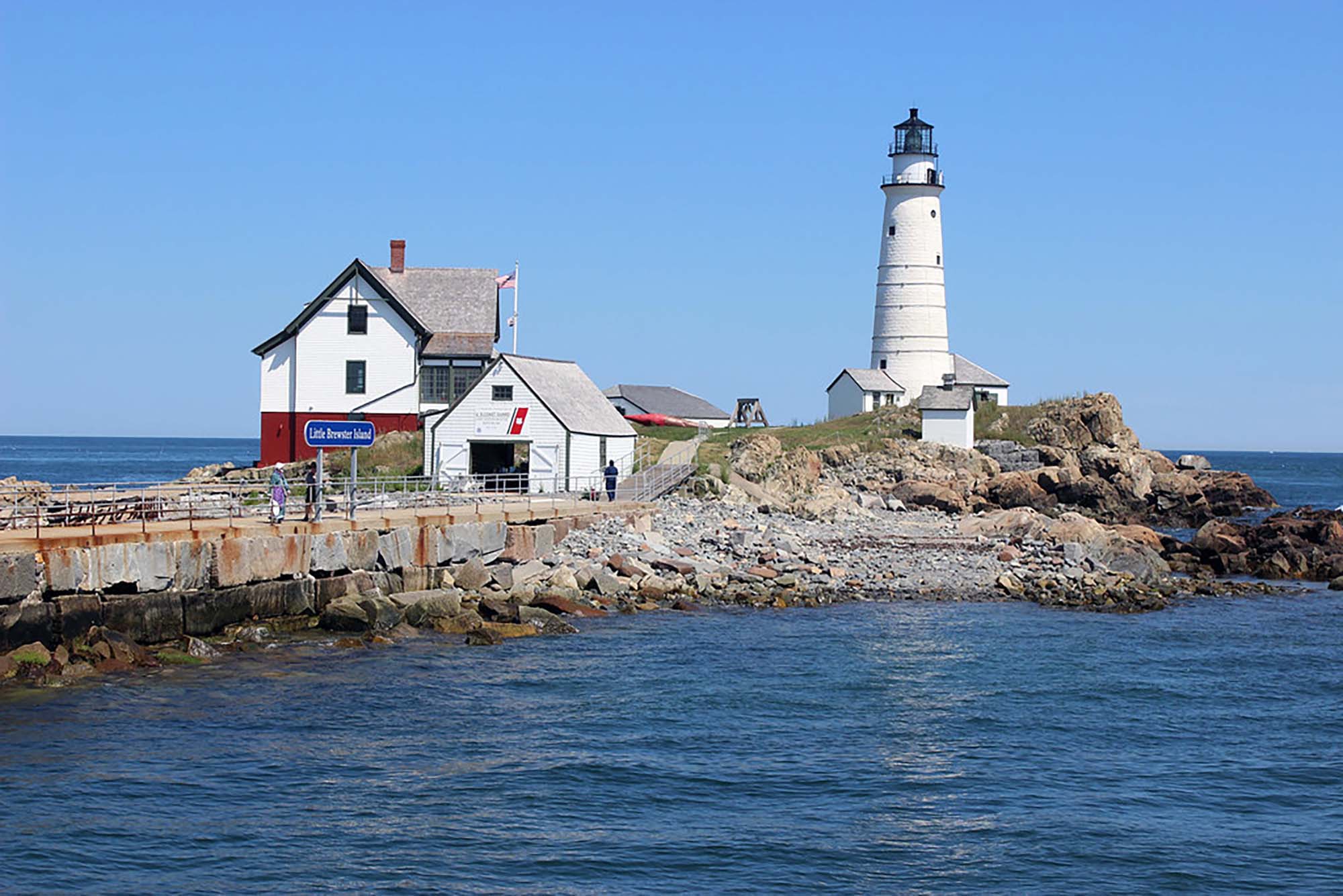 Photo of Little Brewster Island. A small, white lighthouse and house sit on a small island surrounded by a large body of water.