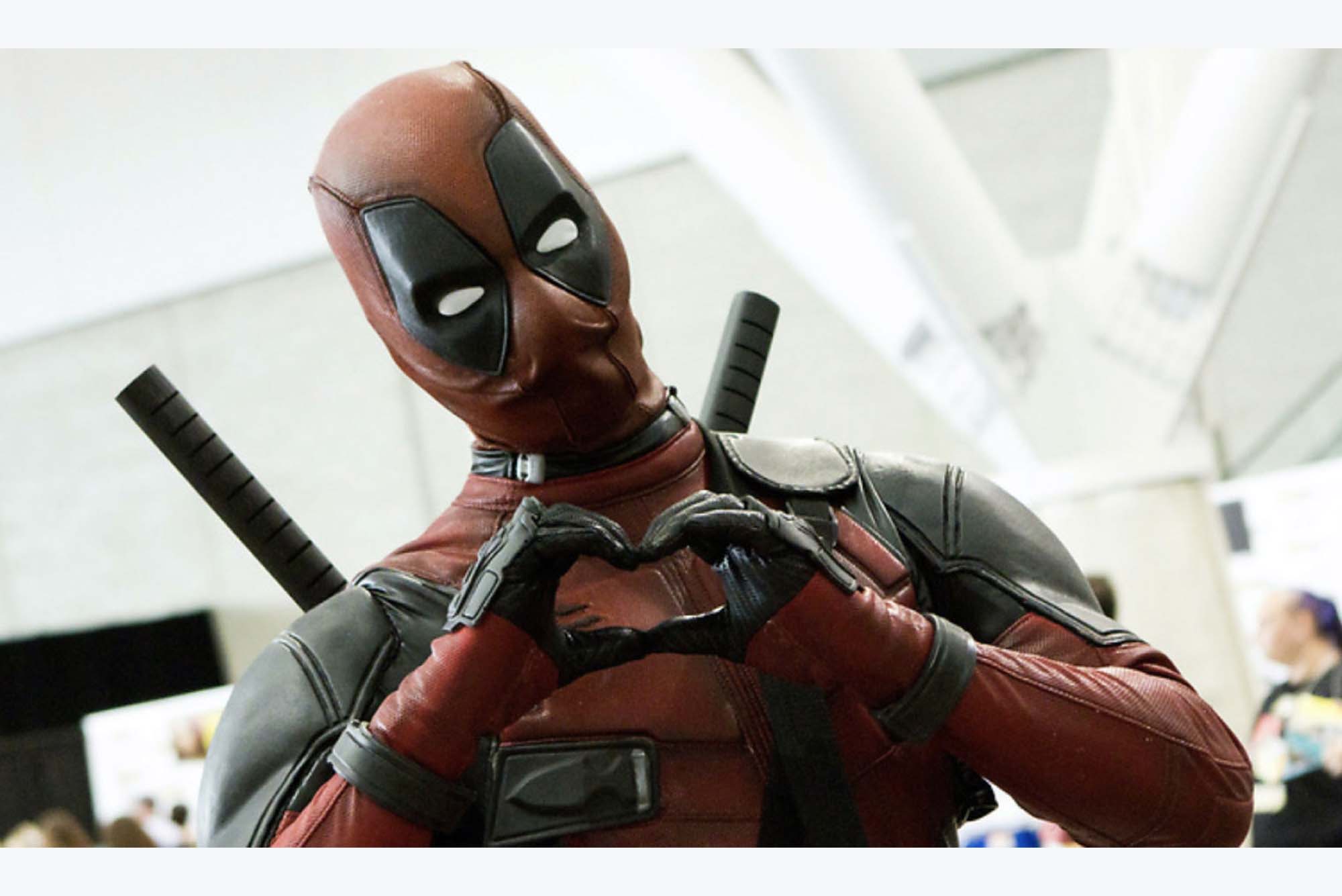 Photo of an attendee of Fan Expo Boston dressed up in a Deadpool costume, i.e. a red and black body suit that covers the person's face and has two white ovals for eyes. The person makes a heart shape with their hands.