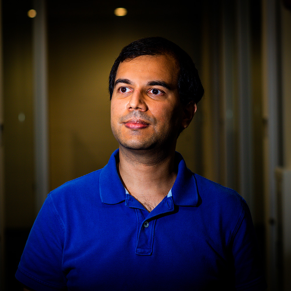 Photo of Mayank Varia, associate professor in the Faculty of Computing & Data Sciences, posing for a photo in an empty hallway. A middle-aged man stands in lit hallway looking tot he left. He wears a blue collared shirt and smiles.