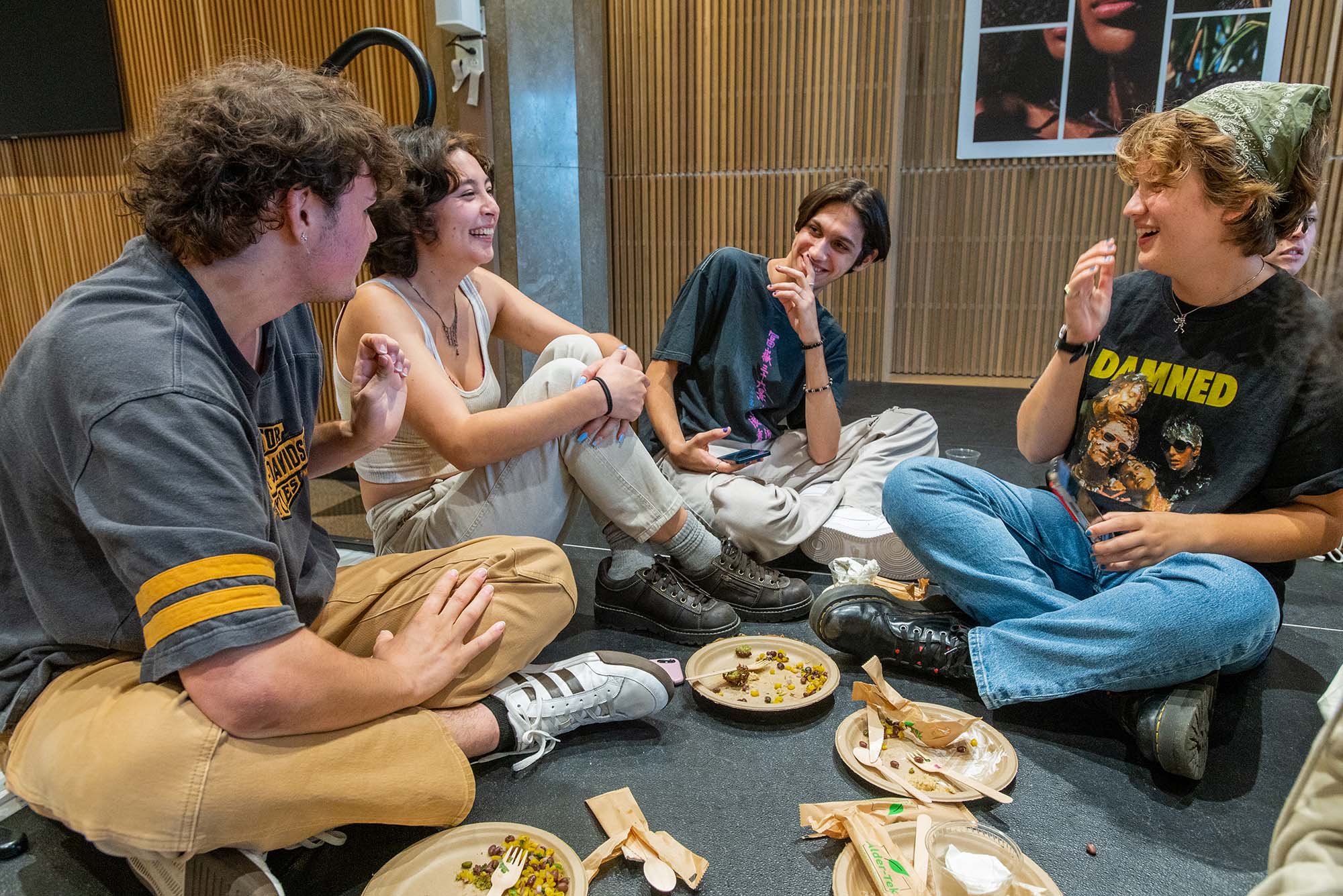 Photo: Alessandro Sitaras (CAS’24), from left, Portia Lee (CAS’24), Miguel Feliciano (CAS’26), and Poppy Livingstone (CAS’26) all sit on a rugged floor and laugh and chat together. Empty paper plates lay in front of them.