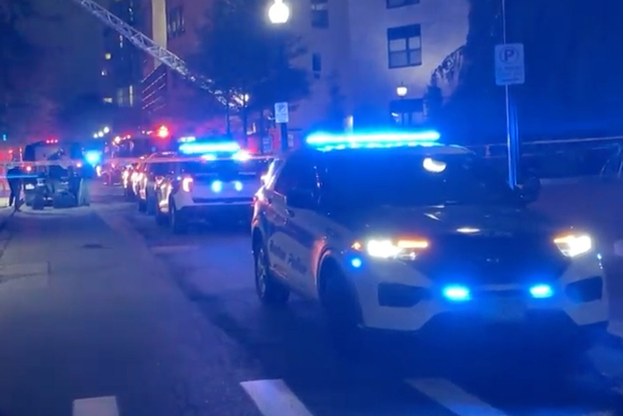 Screenshot of the scene of the package explosion at Northeastern. The scene is tinted blue form police cars and emergency vehicles blocking the street as officials work on the scene.