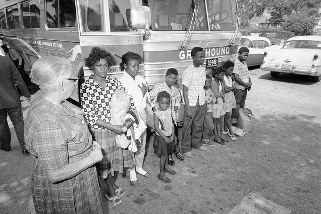 Black and white photo: Eliza Davis of Cuba, Ala., and her eight children ranging in age from 5 to 17, weary and tired on their arrival in Hyannis, Mass. from the south, June 1, 1962. They stand in front of an old Greyhound bus as a white woman to their left looks on.