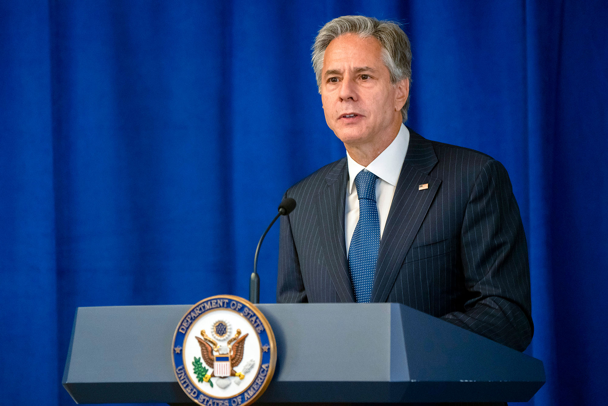 Photo of Secretary of State Antony Blinken speaking about the launch initiative to support Afghan women during the 77th session of the United Nations General Assembly in New York, Sept. 20, 2022. An older white man with graying hair stands in front of a blue curtain at a lectern with the US Government insignia on it. He wears a dark gray suit and blue tie.