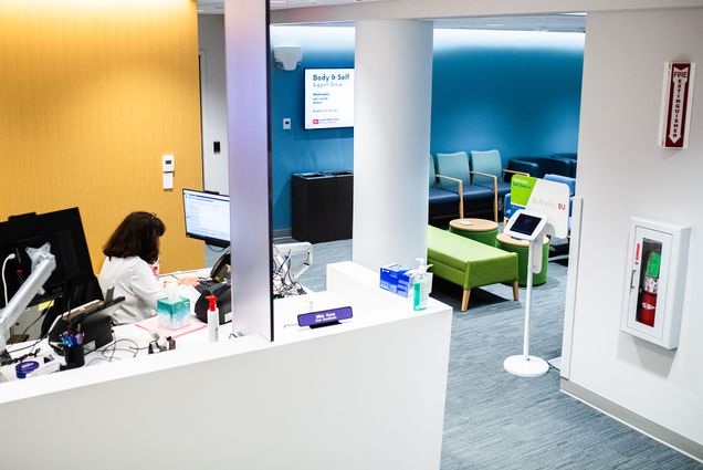 The Student Health Services facilities have been upgraded and have a lot of new, improved, and expanded services to offer to students. Here the lobby is pictured with yellow and blue walls and a receptionist sitting at a computer