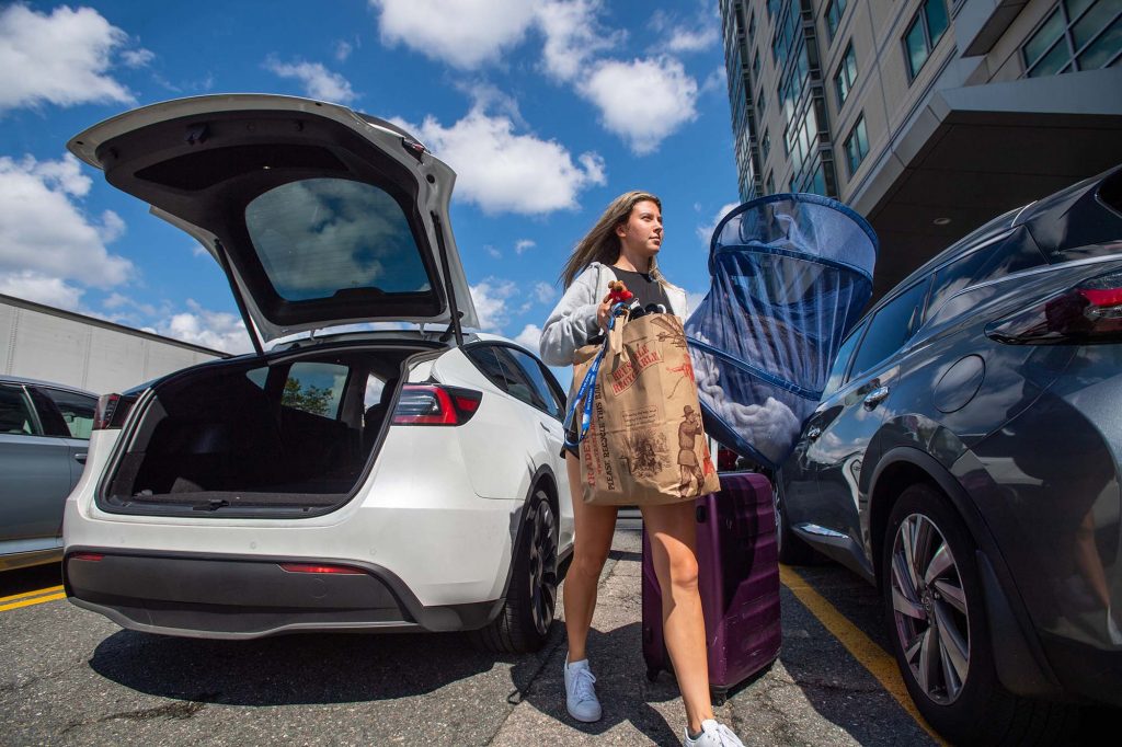 Photo: Michelle Kleyn (SAR’25) unloads her parents’ car after driving with them from New York to move in to her StuviII apartment. A young white woman carrying paper Trader Joe's bags and rolling a large purple suitcase walks between two cars with doors and trunks open. 