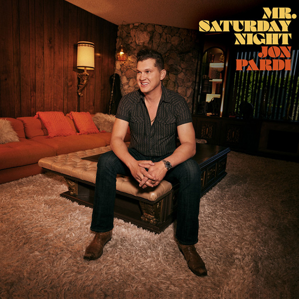 Album cover shows Jon Pardi sitting on living room table and looking to the left. A white man wearing a grey shirt and black pants smiles with hands clasped in front of him as he sits. Title reads "Mr. Saturday Nigh, Jon Pardi"