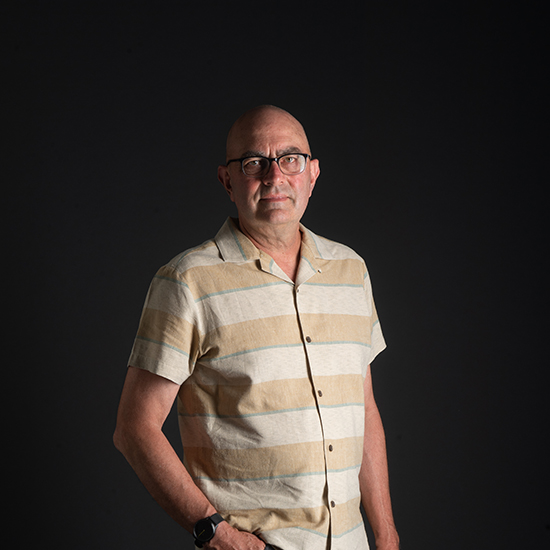a photo of Professor Patrick Kinney of SPH. He wears a striped yellow shirt and stands in front of a black studio backdrop with left hand in his pocket