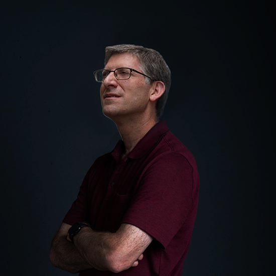 photo of Professor of Environmental Health, Jon Levy, as he poses in front of black backdrop looking off into distance with arms crossed.
