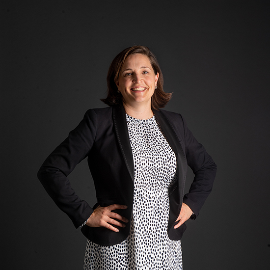 photo of Katharine Lusk, Co-Director, Initiative On Cities. She stands with hands on hips wearing a white pola dot dress and black blazer.