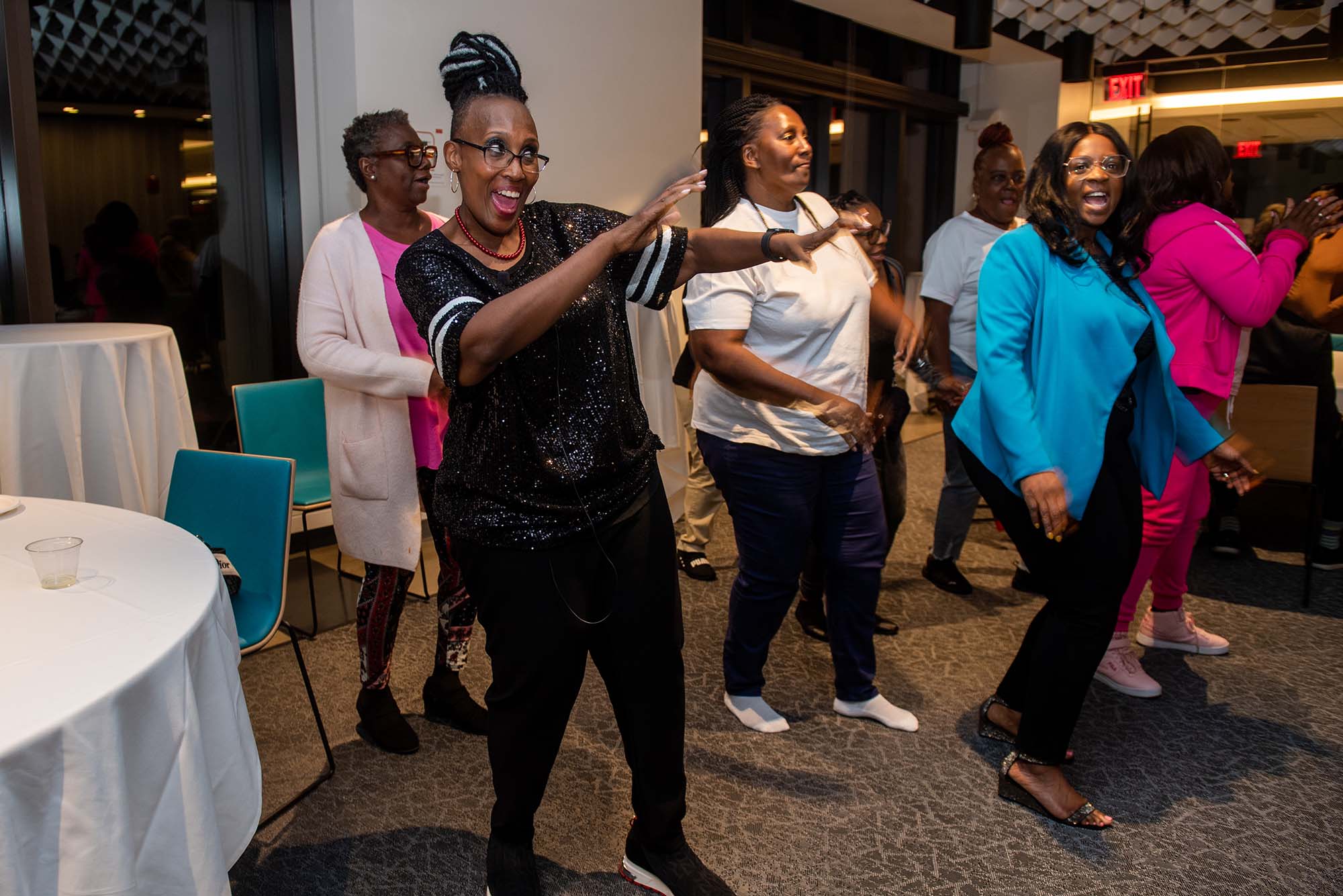 Photo: MC Amanda Merrick, dressed in black, dances with other members during the opening reception for Mothers for Justice & Equality's seventh annual national conference Oct 12 at Howard Thurman Center. A group of Black women gather and dance the cha cha slide.
