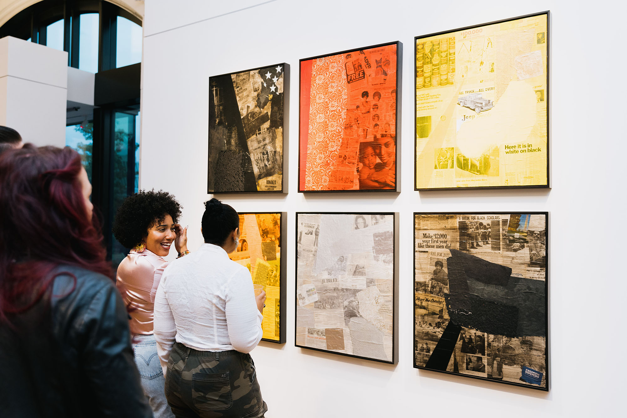 Photo of patrons looking at a gallery wall of large, colorful collage-style artworks.