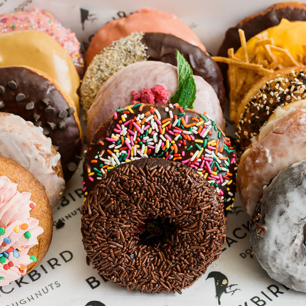 Photo of a box of assorted donuts. Parchment paper on the bottom reads "Blackbird Donuts"