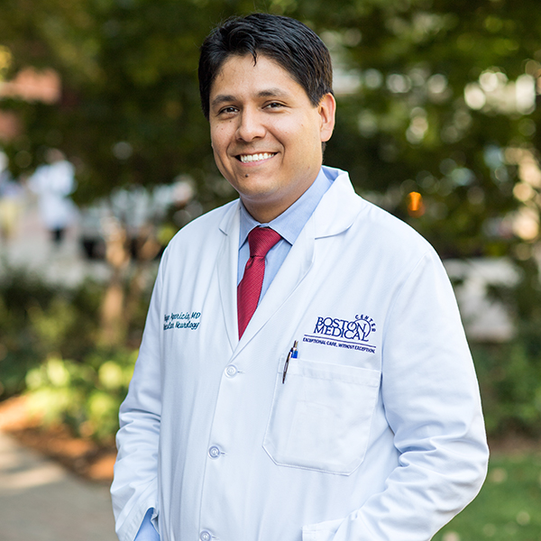 Photo of Hugo Javier Aparicio. A Latino man wearing a light blue collared shirt, red tie, and white lab coat poses for a photo with hands in pockets.