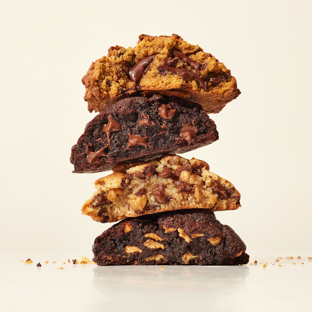 Photo of four large, chunky cookies broken in half and stacked on top of each other. Cookies photographed on a light yellow background.