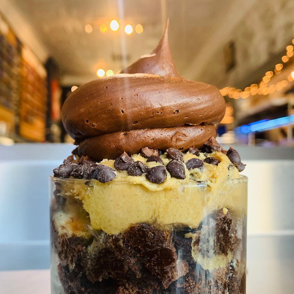 Photo of a small clear cup filled with layers of chocolate cake, chocolate mousse, chocolate icing, and chocolate crunchies.