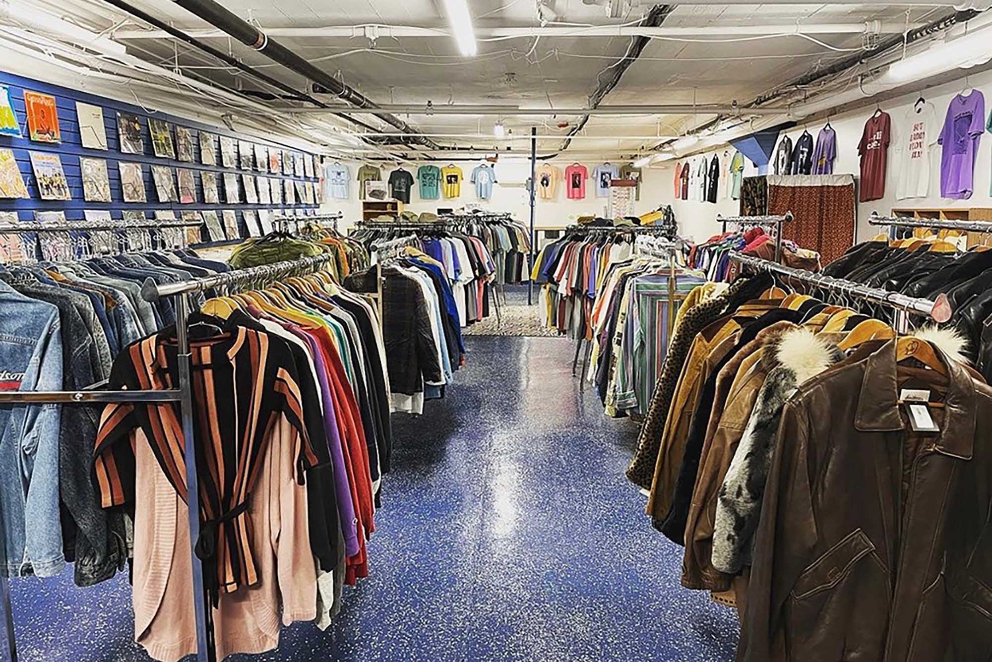 Photo: A shot of the clothing racks The Vintage Underground. The left and right are lined with clothing on hangers, while the interior was blue with overhead lighting.