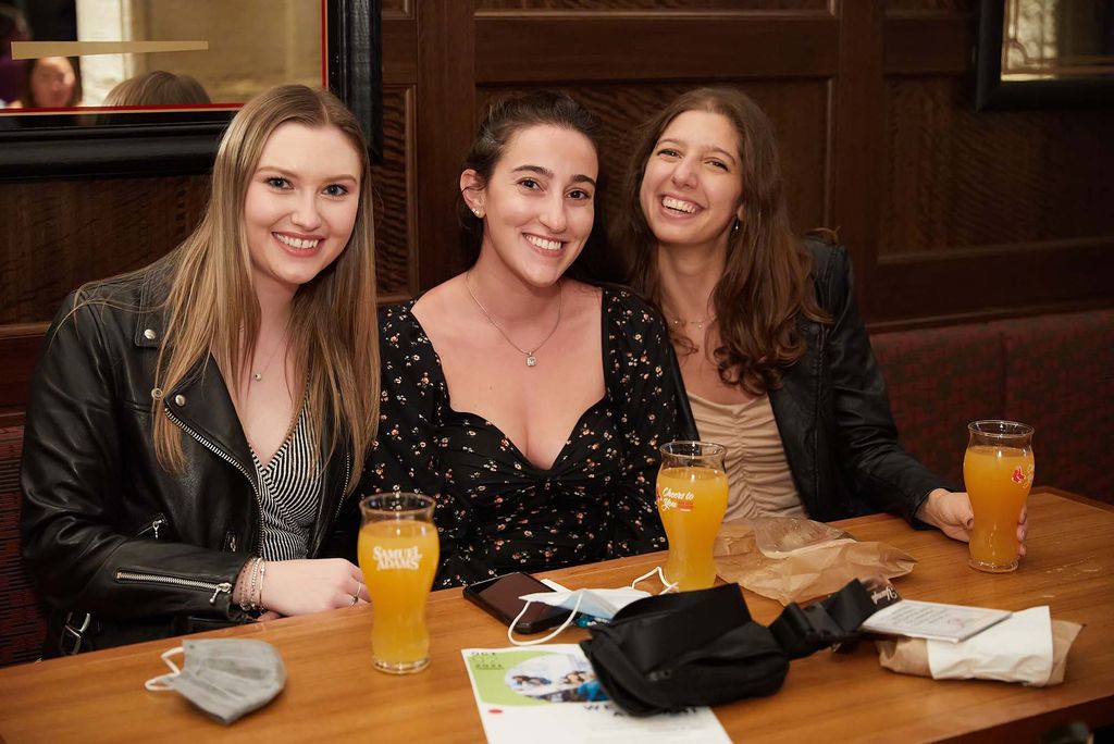 Photo of a group of young alumn, three young women, drinking beers, during Young Alumni night presumably.