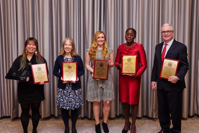 Photo: Perkins Award Ceremony for 2020 and 2021 winners held on November 10, 2022 in the Metcalf Trustee Ballroom. Perkins award winners from left: Lena Landaverde, Aline Hillman, Kimberly Crosta, Ridiane Denis, and Colin D. Riley. Each person holds up a gold plated plaque in front of a grey stage.