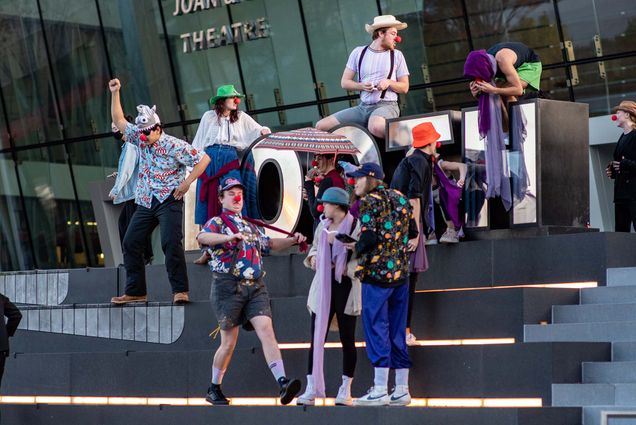 Photo: Students of the CFA TH 331 Movement 3 class climb and walk around the Booth Theatre sign on Commonwealth Ave on Friday, Nov. 4, 2022. A group of students dressed in various clown outfits and red noses goof and play around a large sign letters that read "BOOTH".