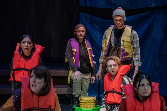 Photo: A cast of people stand on stage wearing multicolored life vests. They have varying looks of shock and awe on their faces.