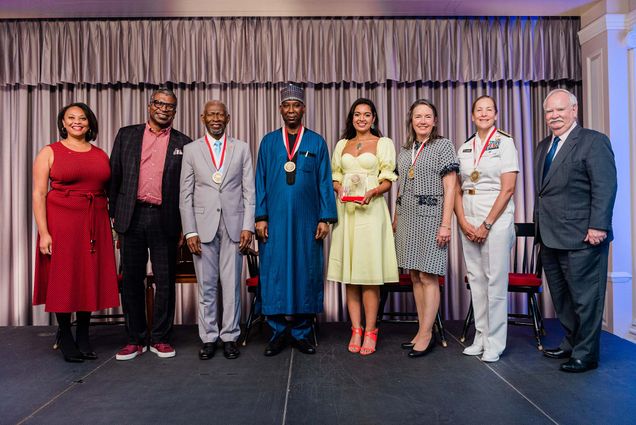 Photo of the winners of the BU Alumni Awards on stage with their medals on (from left): Erika Jordan, BU vice president for alumni engagement; Anthony Harrison (COM’81), president of the Boston University Alumni Association; Lawrence Carter (STH’68,’70,’79), dean of the Martin Luther King, Jr. International Chapel at Morehouse College; Tijjani Muhammad-Bande (GRS’81), permanent representative of Nigeria to the United Nations; Priyanka Naik (CAS’10), vegan chef and cookbook author; Kathleen McLaughlin (ENG’87), Walmart, Inc., executive vice president and chief sustainability officer and president of the Walmart Foundation; Shoshana Chatfield (Pardee’88), US Navy rear admiral and president of the United States Naval War College; and Robert A. Brown, BU president. Photo by Doug Levy