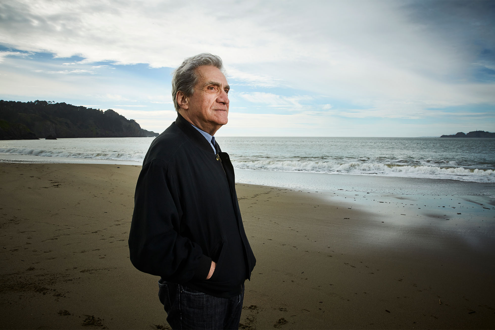 “I had the good luck to be raised among expert joke-tellers, complainers, arguers, schmoozers, boasters, and liars,” Pinsky says in his new memoir, Jersey Breaks. Photo by Gabriela Hasbun. Pinsky stands looking out over an ocean beach on a cloudy day