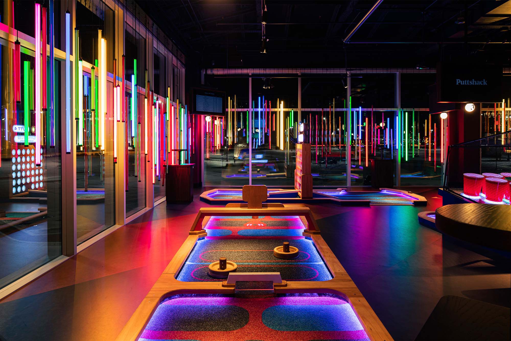 A photo of the inside of Puttshack Boston, with minigolf course greens and fun neon lighting