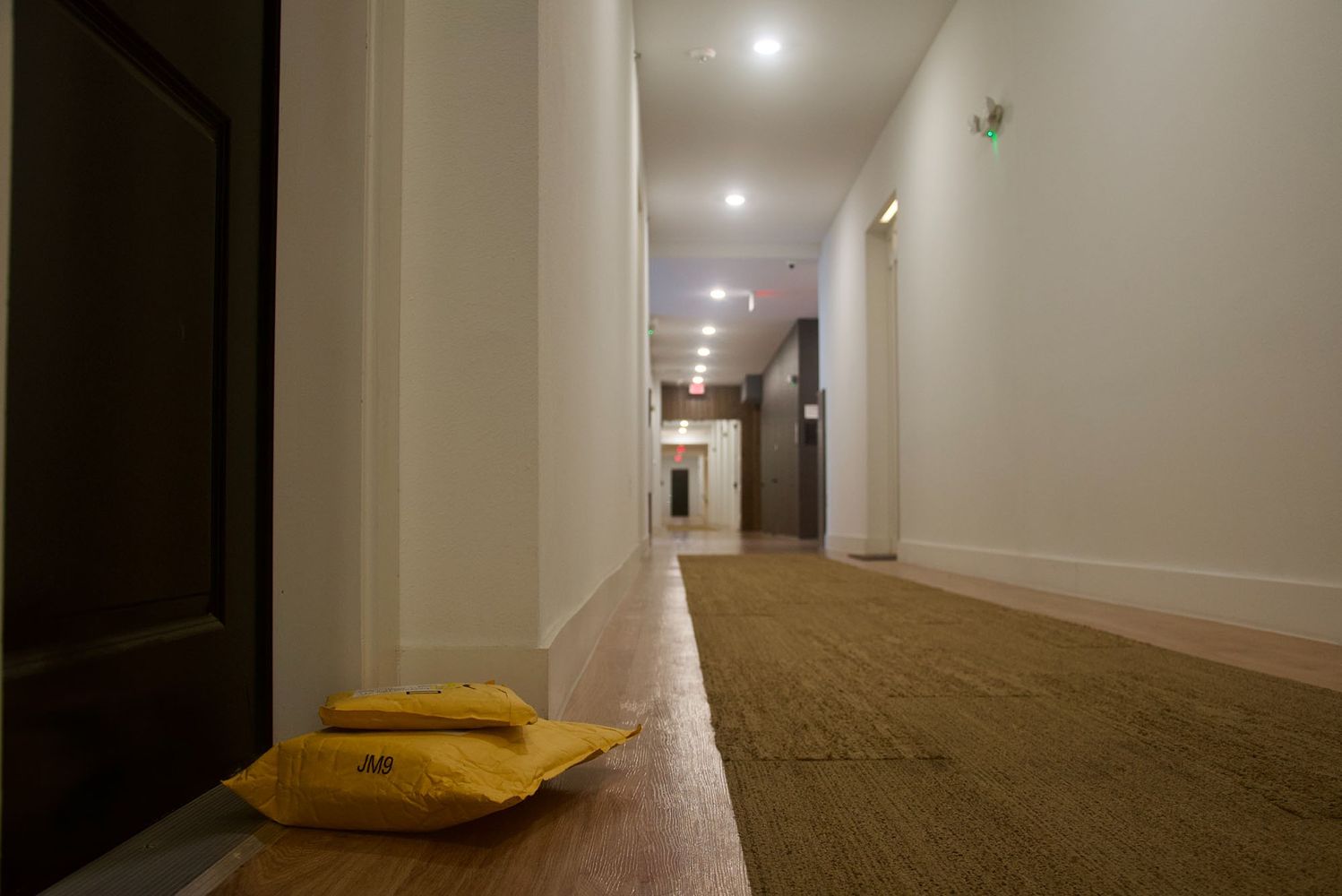 Photo: Two small, stuffed manila packages lay in front of an apartment door in an empty hallway.
