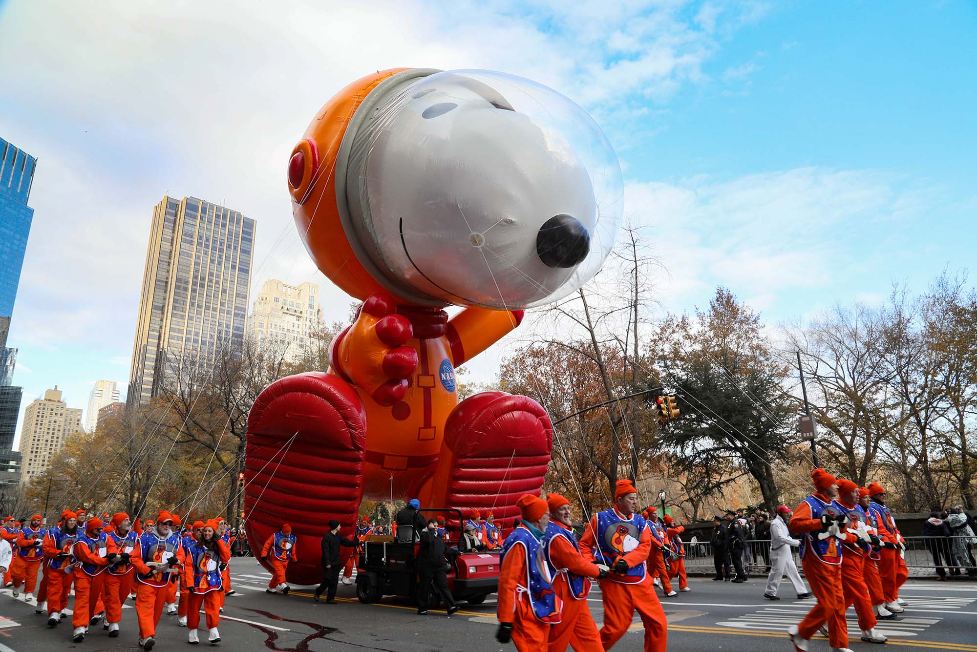 Photo: A large Snoopy Astronaut balloon debuts at the Macy's Thanksgiving Day Parade. A giant Snoopy dog balloon held by a crowd of people in orange outfits below it, makes it way down the street.