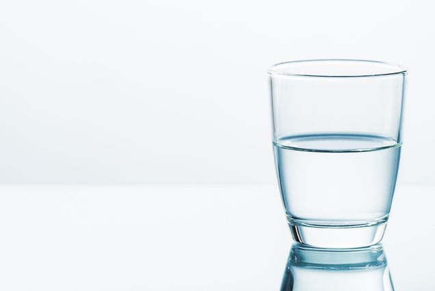 Photo: A glass filled halfway with water on a clear white background.