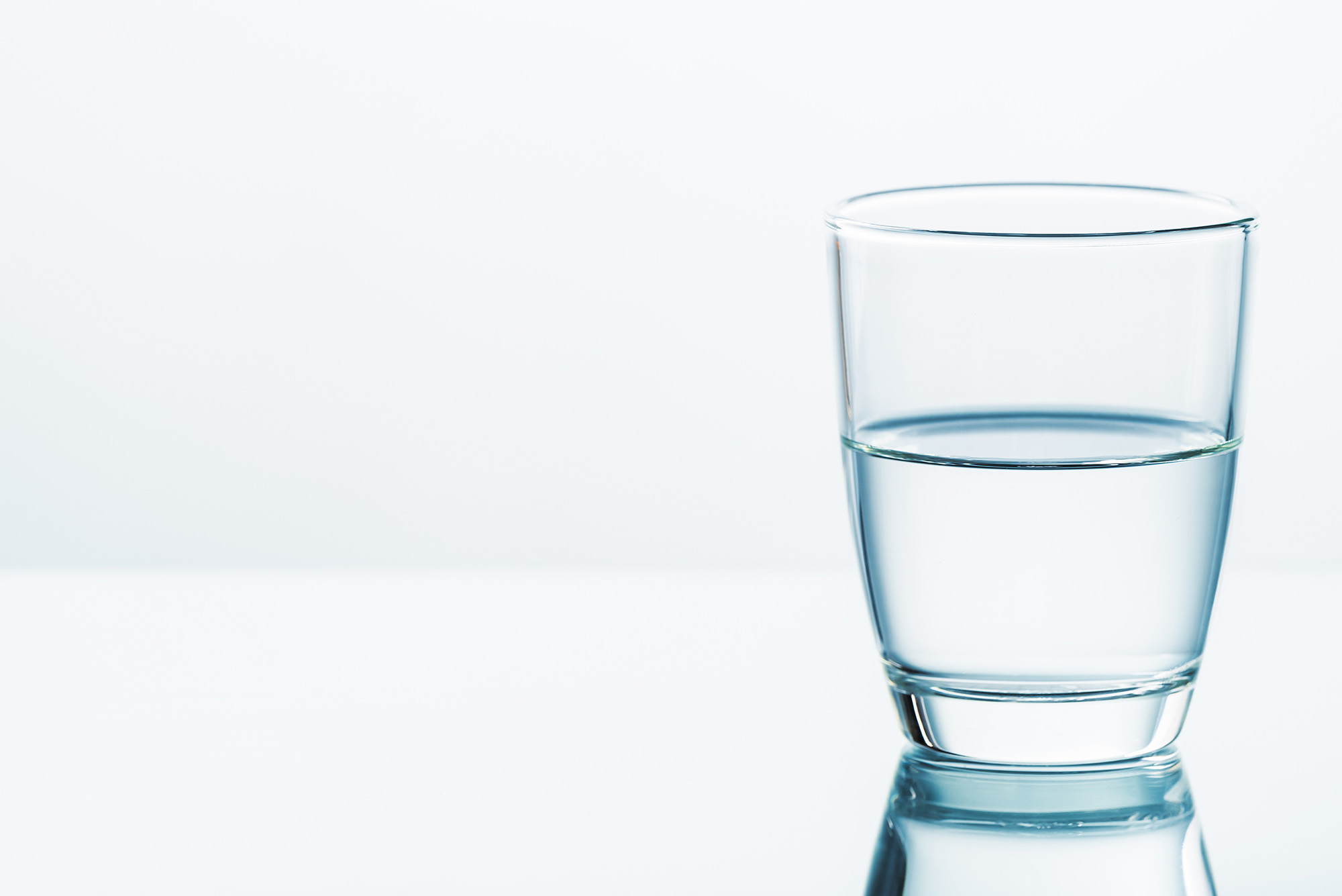 Photo: A glass filled halfway with water on a clear white background.