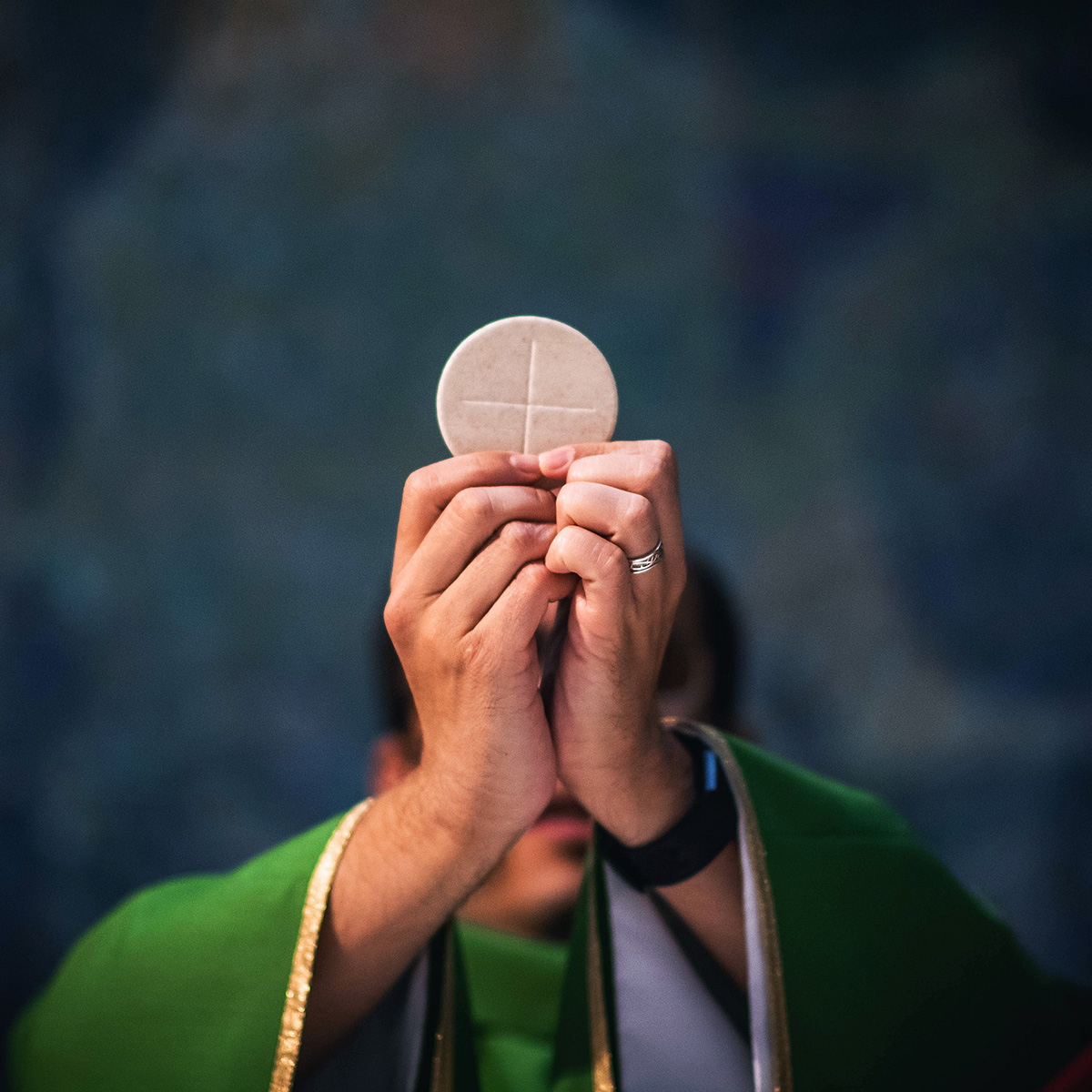 Photo of a priest in a green robe raising communion.