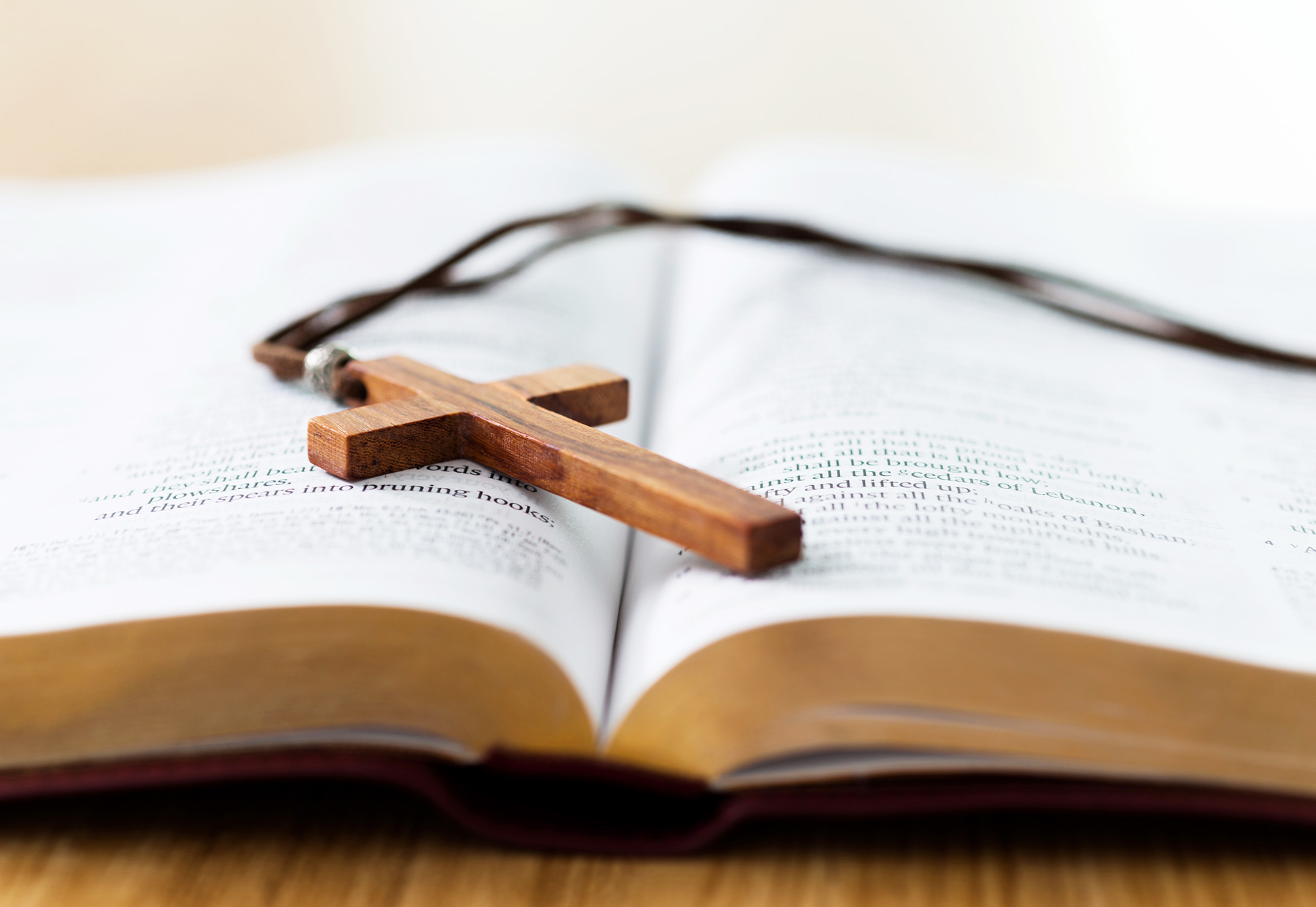 Photo: an open Bible is shown with a small, wooden cross lying on top of the open pages.