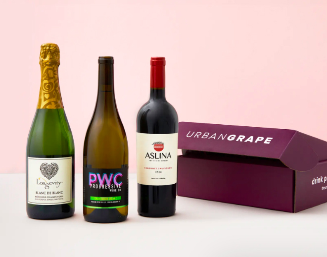 Photo: Three bottles of wine are arranged on display next to a dark purple box engraved with with silver letters that read "Urban Grape". They all are displayed on a light pink background.