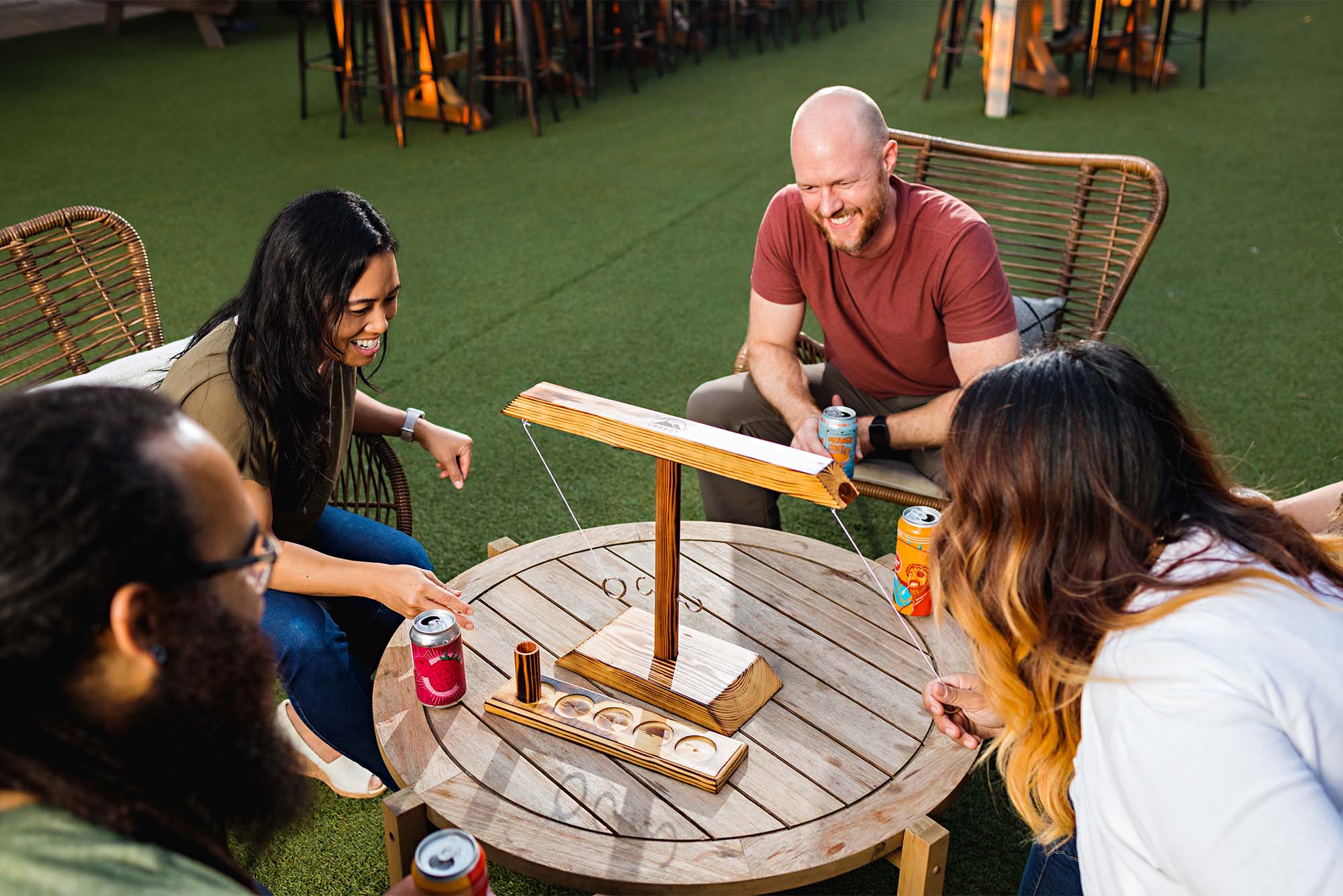 A group of people sit around a patio table with a Craggy Games wood structure on the table.