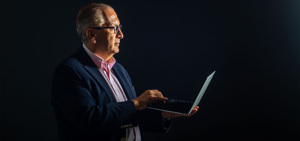 Azer Bestavros, wearing a suit against a black background, holds a laptop