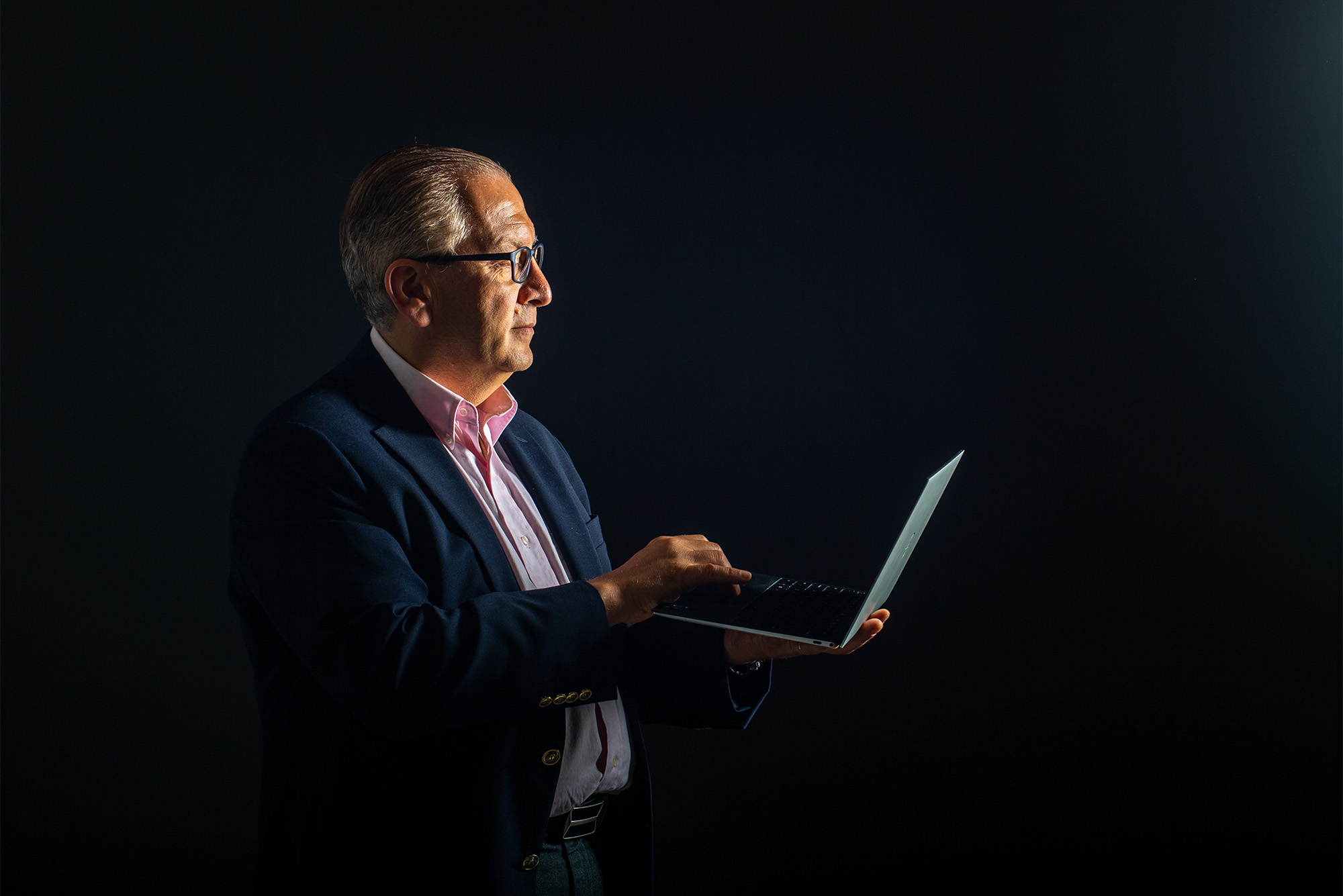 Azer Bestavros, wearing a suit against a black background, holds a laptop