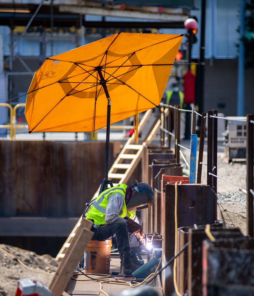 Photo: The data Science construction continues on the corner of Bay State Rd and Granby Street August 31. A masked metal worker is shown welding something as sparks fly around him. A large orange umbrella is open above him.