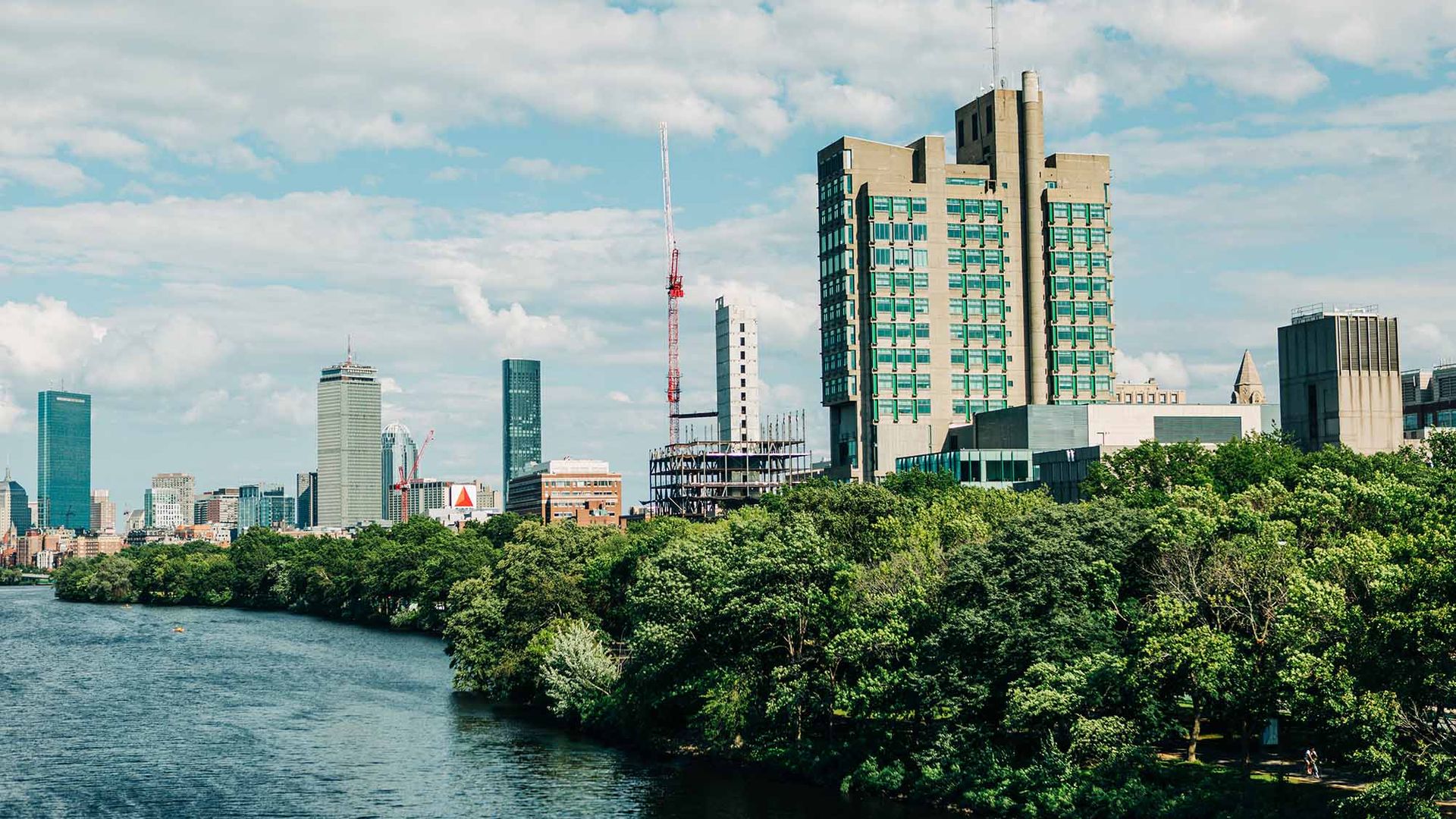 Photo: Boston University's campus along the Charles River on a sunny day. The beginning profiles of the Center for Data Sciences' structure can be seen in progress amongst the buildings.